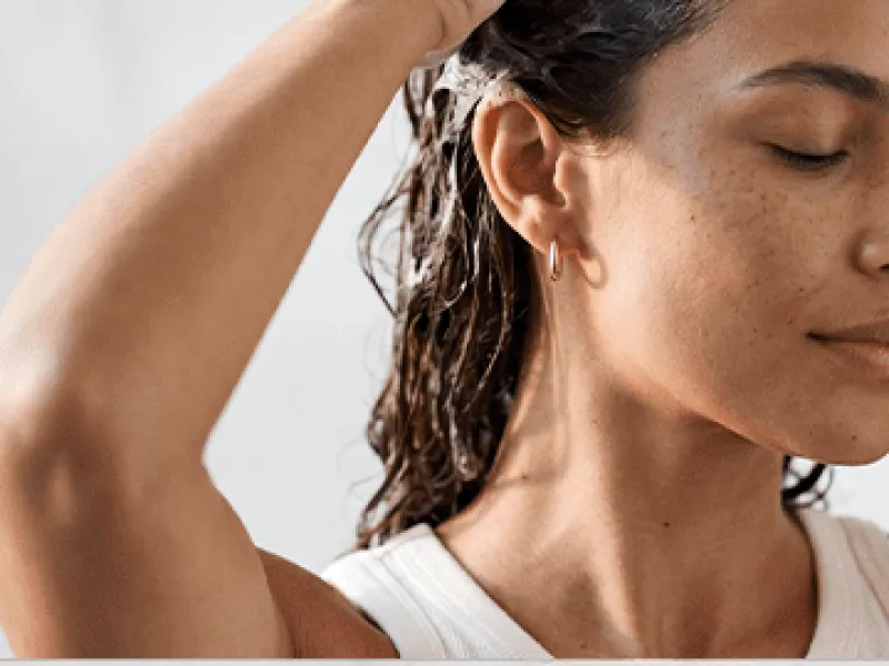 Mulher no chuveiro massageando o couro cabeludo com espuma de shampoo