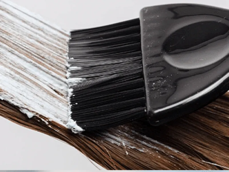 Pincel de coloração distribuindo o produto branco mecha a mecha num cabelo castanho